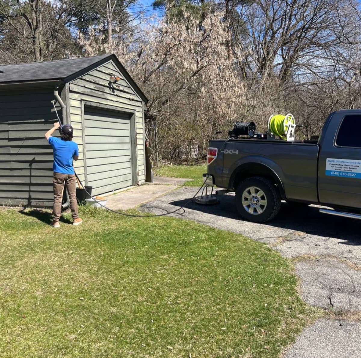 Angelo washing a garage exterior with his equipped work truck on site