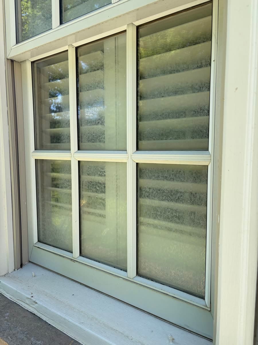 Window with cloudy, spotted panes in front of interior shutters